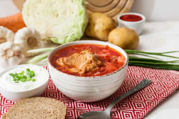 Bowl of tasty borscht and ingredients on table