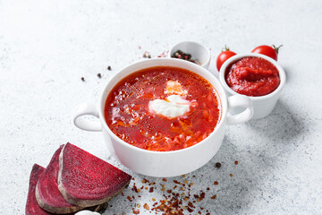 Pot of tasty borscht and ingredients  on light background