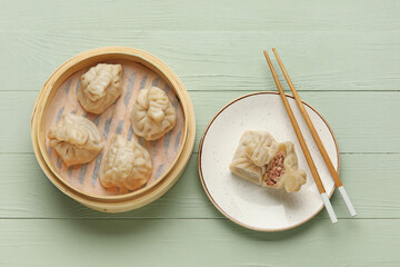Bamboo steamer and plate with tasty dumplings on color wooden background