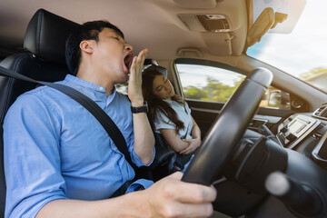 sleepy man yawning while driving car and his wife is sleeping