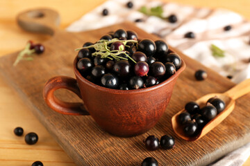 Cup and scoop with ripe black currant on wooden background