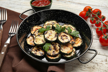 Frying pan with tasty grilled zucchini on light wooden background