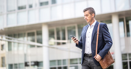 Man in casual business attire checks his phone walking outdoors in an office buildings environment