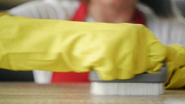 Young housewife in yellow rubber gloves scrubs a stain on the countertop with effort.