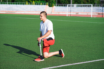 Obraz premium Young caucasian brunette male with prosthetic leg doing lunge at the stadium on the field. Sport concept