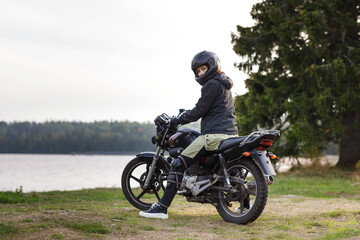 Fototapeta na wymiar biker girl in black clothes and black helmet on a motorcycle