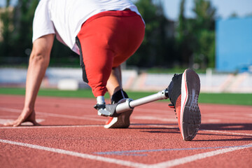 Caucasian male athlete with a prosthetic leg standing at the start on the track at the stadium. Back view. Sport concept.