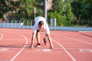 Obraz premium Caucasian male athlete with a prosthetic leg standing at the start on the track at the stadium. Sport concept.