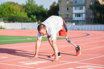 Fototapeta premium Caucasian male athlete with a prosthetic leg standing at the start on the track at the stadium. Sport concept.