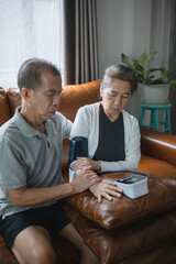 Asian senior couple checking blood pressure at home, after the blood pressure gauge shows the result they shocked.