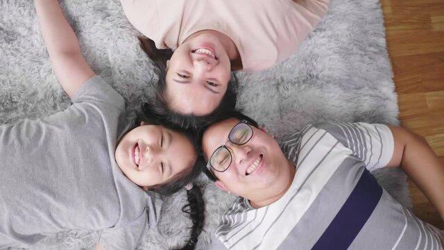 Top view of happy Asian family lying on the floor in living room and looking at camera, smiling and getting happy. Staying with family at home in the weekend. Happy family concept