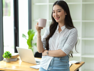 Success young businesswoman hold coffee cup and smile to camera in modern office