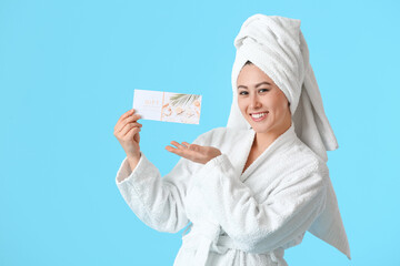 Young Asian woman with gift certificate for massage on color background