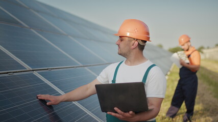 Engineer standing with Solar cell panels looking monitor of the Electric power value made from the solar cell. Man holding laptop in her hands standing on field with solar panels. Solar energy