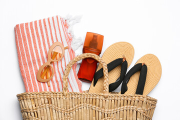 Stylish bag with beach accessories and sunscreen on white background