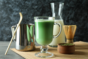 Cup of matcha latte and accessories for making on gray textured table