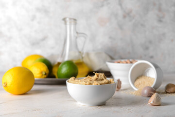 Bowl with tasty hummus and garlic on light background