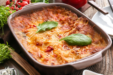 Baking dish with tasty vegetable lasagna on wooden background