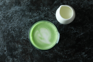 Glass of matcha latte and milk on black smokey background