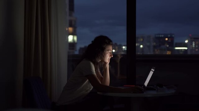 The girl works on a laptop in the late night on a high floor. Late finishing project. Deadline of delivery of the project.