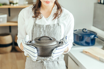キッチンで女性がミトンをつけて両手で鍋を持っている　woman kitchen