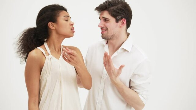An emotional woman swearing to the camera while a man trying to calm her down standing isolated over a white background in the studio
