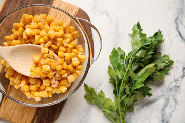 Bowl with corn kernels and parsley on light background, closeup