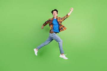 Full length profile photo of hooray brunet young guy jump wear shirt jeans sneakers isolated on green background