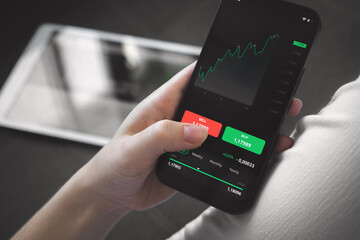Stock market trading at home. Person using mobile phone with financial graphs for investement, buying and selling