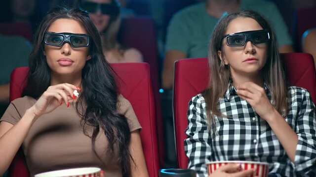 Two female friend watching film premiere in 3d glasses with shocked face expression sitting at row 