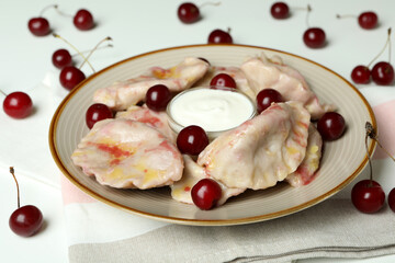 Plate with pierogi with cherry on kitchen towel on white background