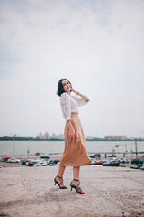 A happy girl on the river bank, standing on the bridge, smiling, a girl walks on the bridge by the river. Freedom. The wind is blowing the girl's hair.