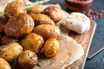 Board with baked potatoes and rosemary on dark background
