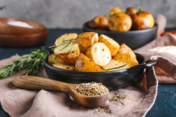 Frying pan with baked potatoes and rosemary on dark background
