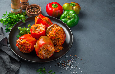 Stewed pepper stuffed with meat and rice on a black plate with fresh herbs on a gray-blue...