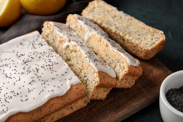 Wooden board with glazed poppy seed cake on table, closeup