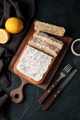 Wooden board with glazed poppy seed cake on dark background