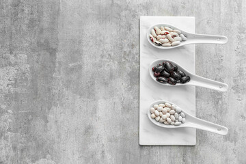 Spoons with different types of beans on grunge background