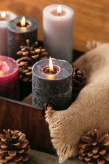 Beautiful burning candles in wooden box and pine cones, closeup