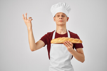 male baker in a white apron holding a loaf in hand cooking food