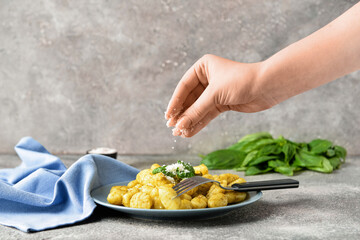 Woman decorating tasty pesto gnocchi with cheese on grey background, closeup