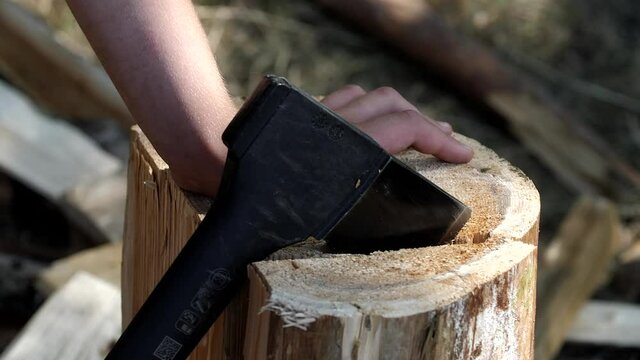 Logging wood. Strong male hands chipping off a piece of log with an ax close up. Man in the forest is trying to split a log with a cleaver. Cutting wood with a large sharp ax outdoors. 