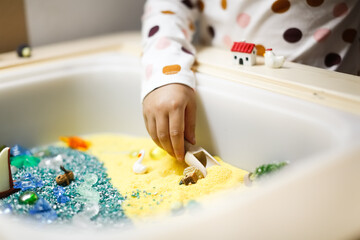 Montessori material. Children's hands play with sand and little toys. Kinetic sand in sandbox. Sensory development.