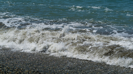 White wave breaking on Sochi Black Sea coast. White spray and foam in foreground. Emerald blue sea water as background for theme of relaxation. Elegant nature concept for design