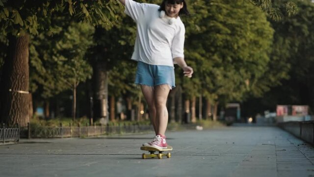 Happy asian girl skateboarding in the park at summer