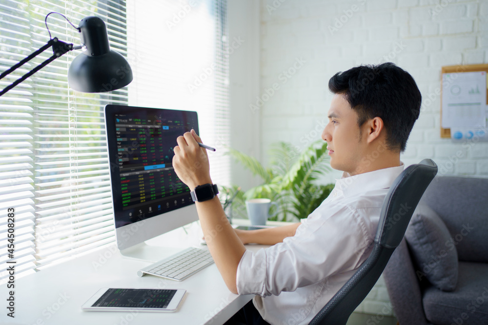 Poster Young trader is pointing at graphs on computer screen and analyzing data while working in his modern office.