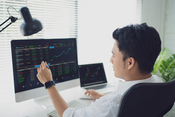 Analyzing data. Back view of young businessman or trader pointing on the data on computer screen with pen while working his modern office.