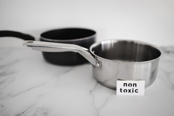 healthy cooking concept, stainless steel vs non stick saucepan side by side with Non Toxic label on...