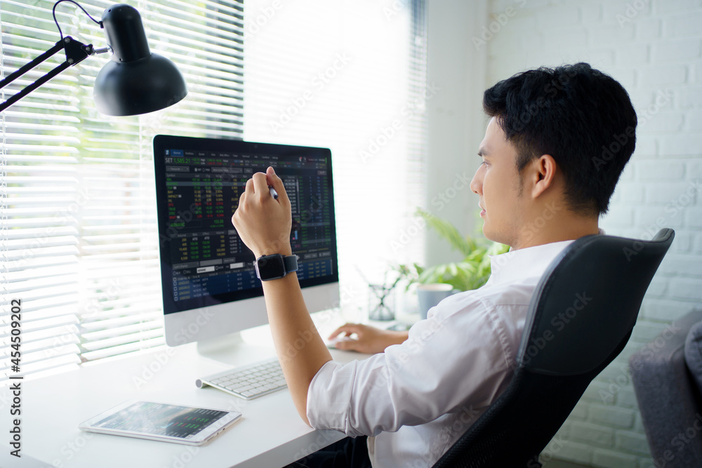 Poster young businessman or trader pointing on the data on computer screen with pen while working. he is an