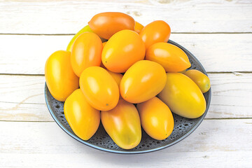 Fresh yellow tomatoes in a dark plate on a wooden background. Autumn harvest.
